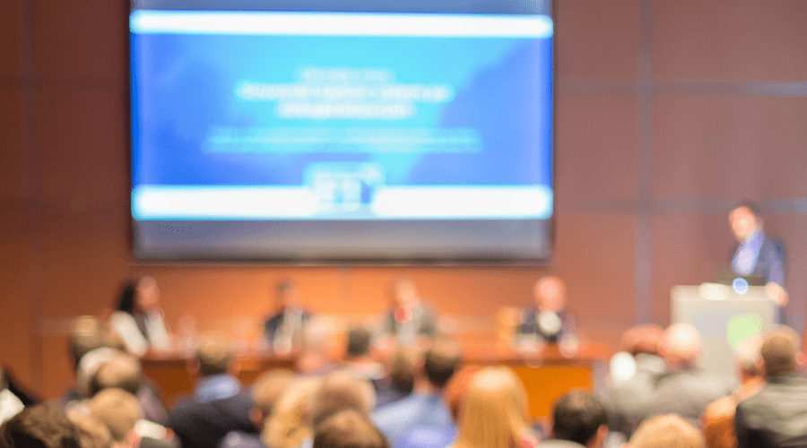 A blurred photo of people attending a conference.