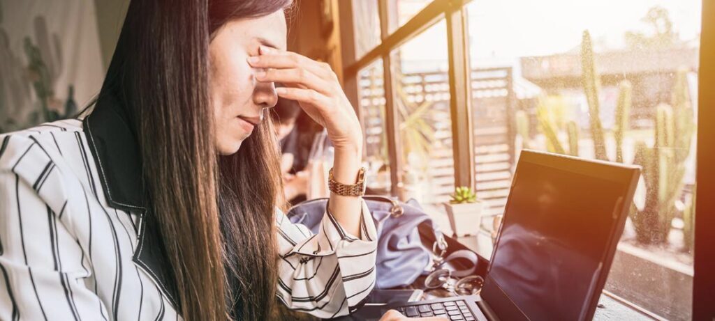 Female dealing with digital eye strain while working at computer and rubbing eyes