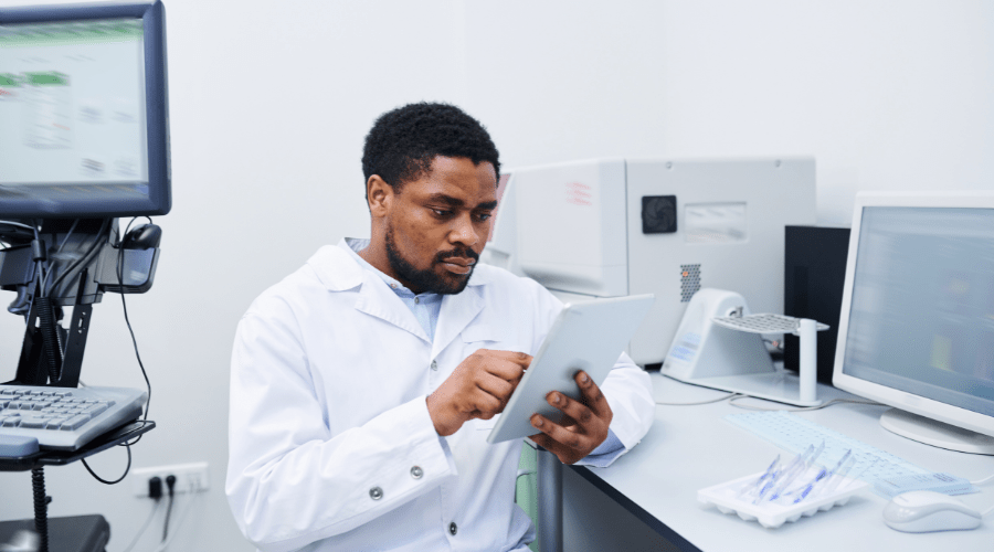 A lab tech uses a tablet to communicate while surrounded by other technology.