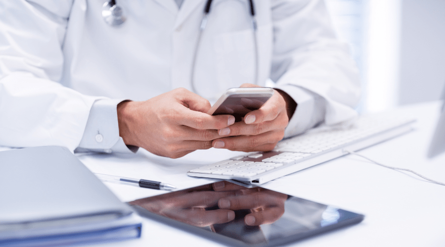 A doctor is overwhelmed with the technology he is using including computer, tablet, and mobile phone.