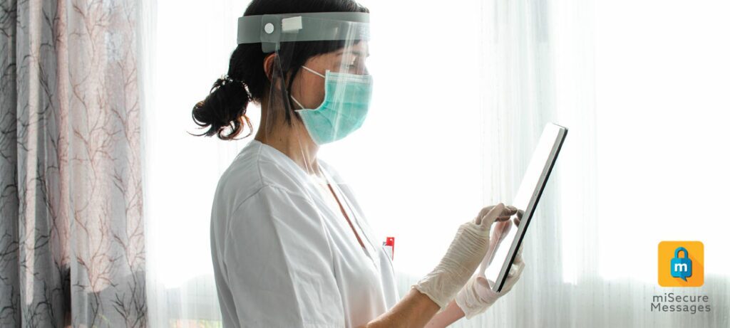 A nurse in PPE uses a tablet to securely message a patient's care team.