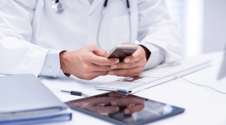 A doctor is overwhelmed with the technology he is using including computer, tablet, and mobile phone.
